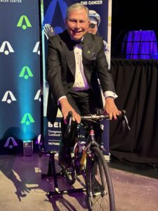 Dr. Weiner rides a bicycle in a tuxedo at the Lombardi Gala